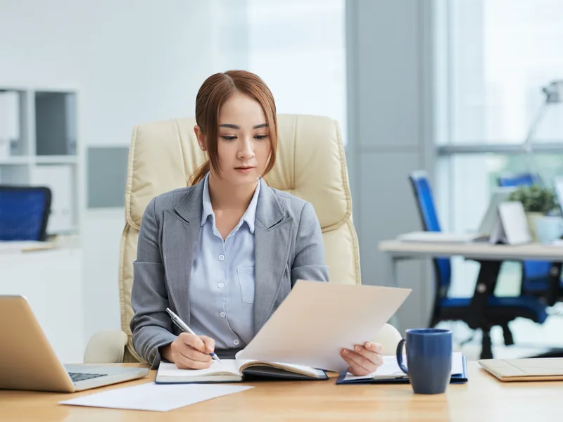 Chuyên viên đối chiếu tài liệu với nguồn trên máy tính và ghi chú lại
